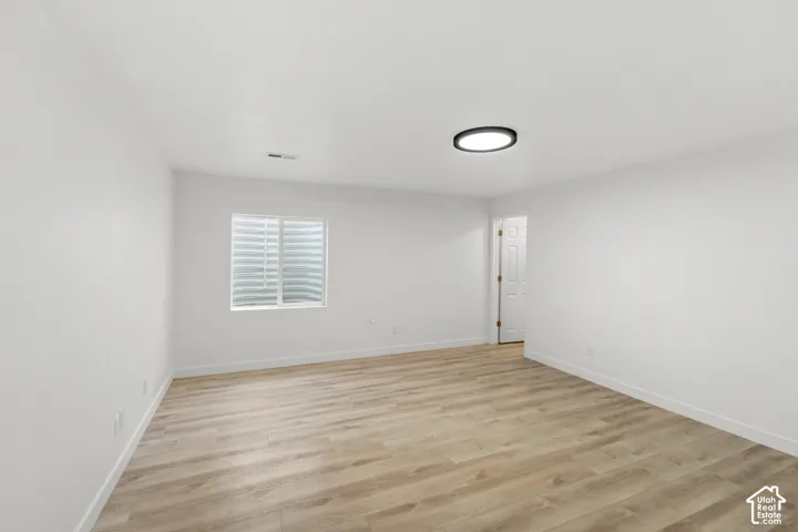 Spacious room featuring wood-finish flooring, white walls, a flush-mount ceiling light, and a window with blinds