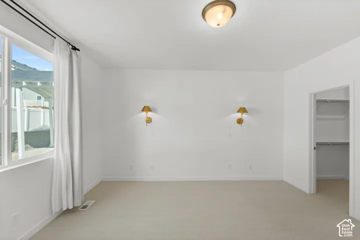 Neutral carpeted flooring, white walls, flush-mount ceiling light fixture, wall-mounted sconce lighting, and a walk-in closet with built-in shelving