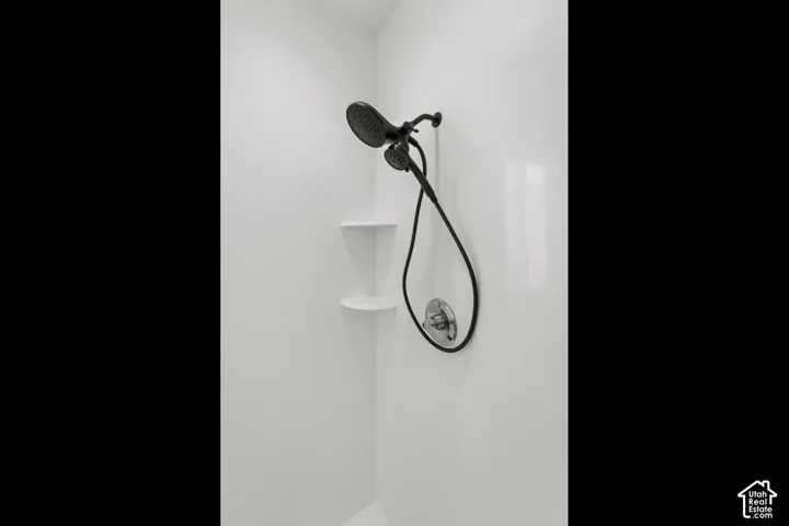 Shower stall featuring a handheld showerhead, a fixed showerhead, and integrated corner shelving