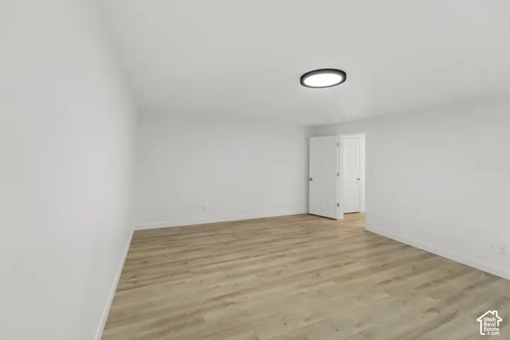 Spacious room with wood-finish flooring, crisp white walls, and a contemporary flush-mount ceiling light