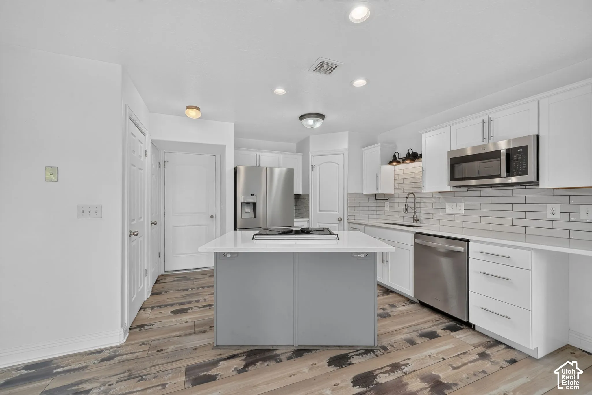 Kitchen featuring white cabinetry, stainless steel appliances, a center island with a cooktop, subway tile backsplash, and wood-finish flooring