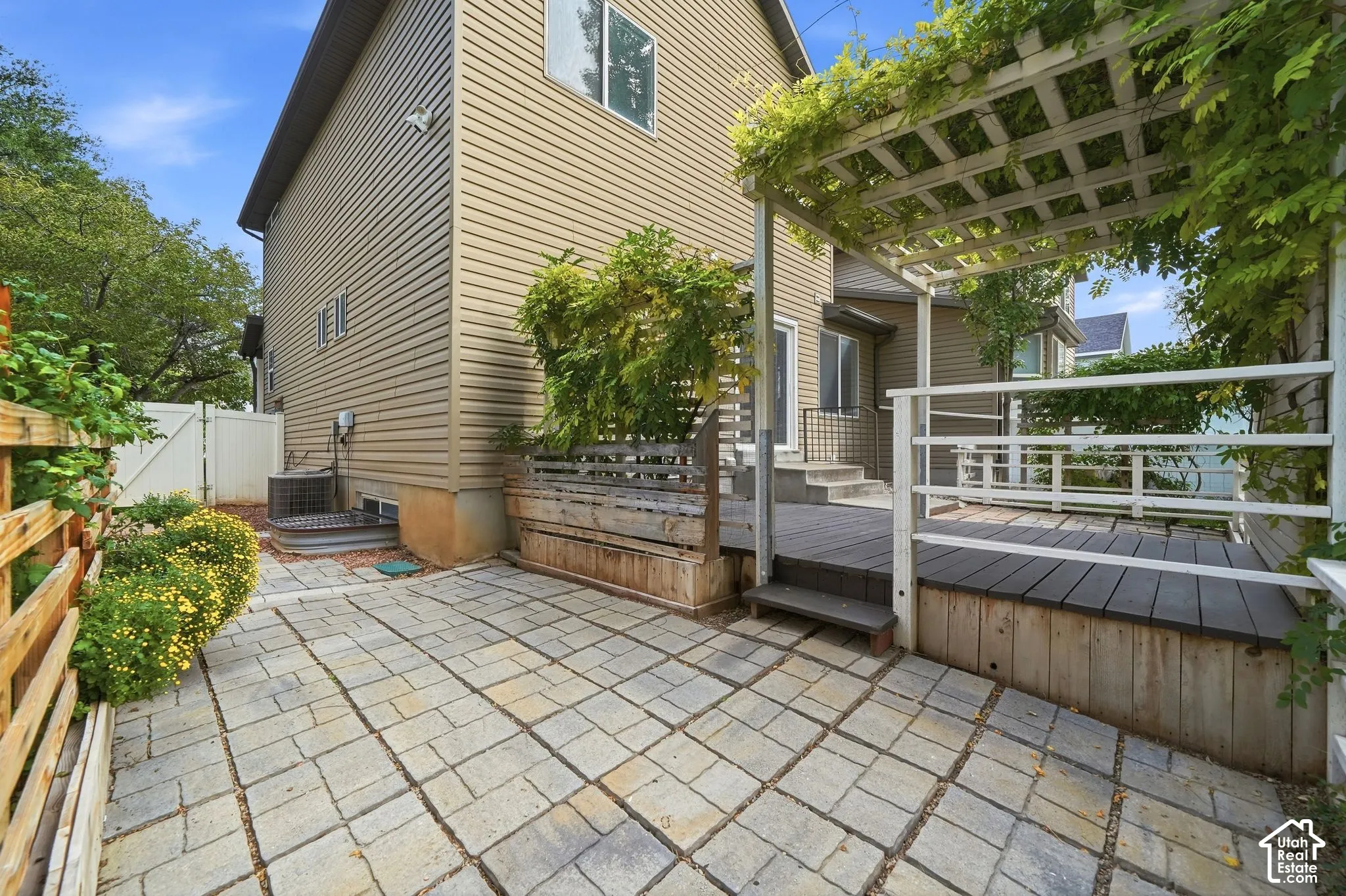 Expansive outdoor space featuring a stone paver patio, a multi-level deck, a wooden pergola with mature vines, and a privacy fence