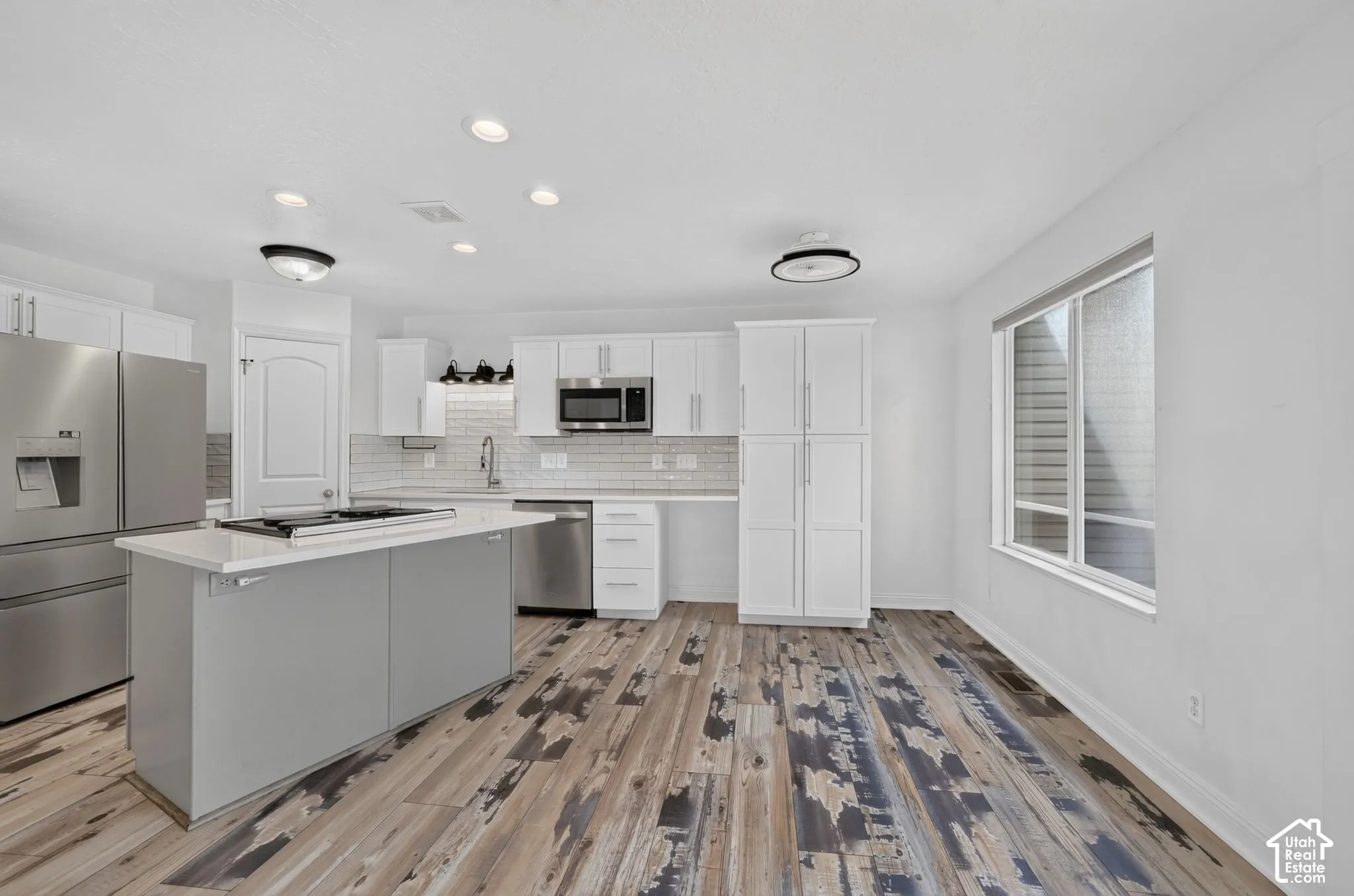 Kitchen featuring white cabinetry, a center island with a built-in cooktop, stainless steel appliances, and wood-finish flooring