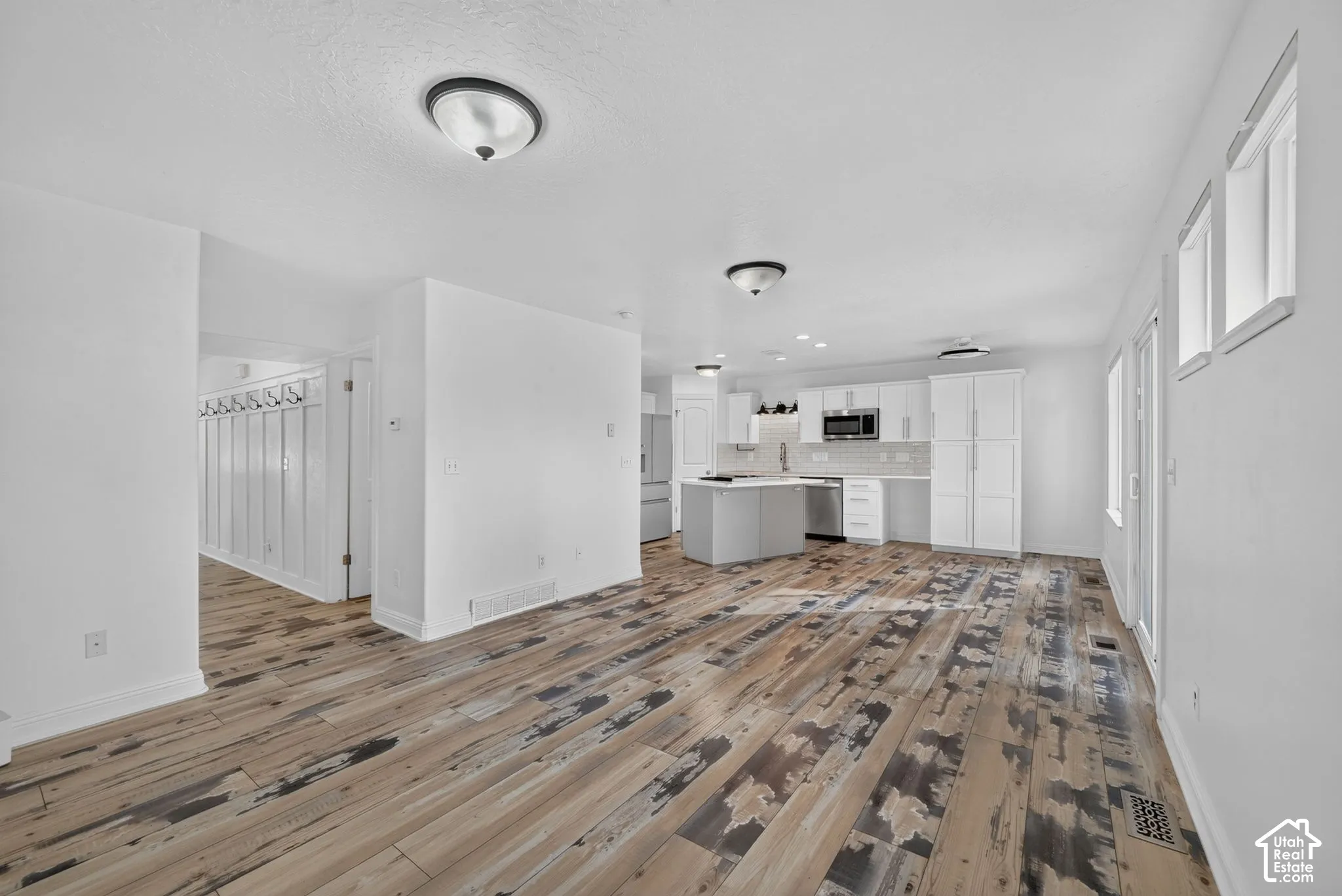Wood-finish flooring, white walls, recessed lighting, white kitchen cabinetry, and a center island with a cooktop