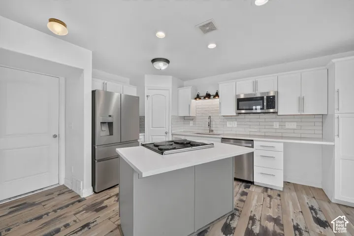Kitchen featuring an island with a built-in cooktop, white cabinetry, stainless steel appliances, white subway tile backsplash, and wood-finish flooring