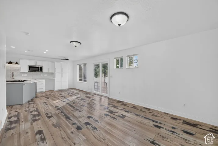 Wood-finish flooring throughout, white walls, and a modern kitchen featuring white cabinetry and stainless steel appliances