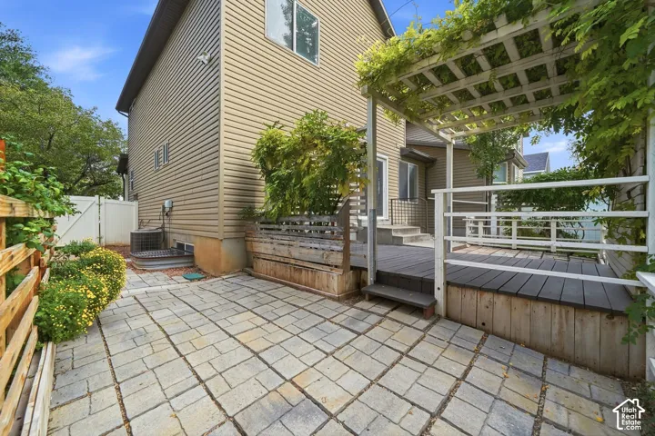 Expansive outdoor space featuring a stone paver patio, a multi-level deck, a wooden pergola with mature vines, and a privacy fence