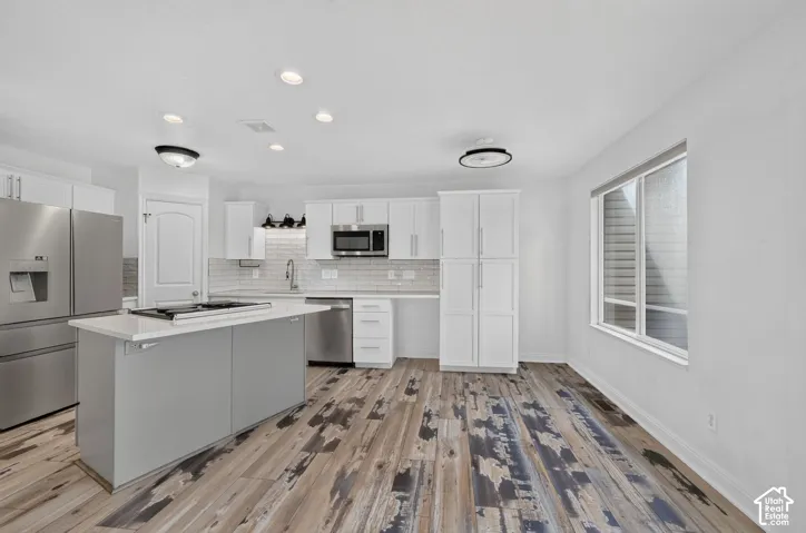 Kitchen featuring white cabinetry, a center island with a built-in cooktop, stainless steel appliances, and wood-finish flooring