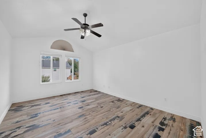 Vaulted ceiling with an attached ceiling fan, large windows with roller shades, and wood-finish flooring