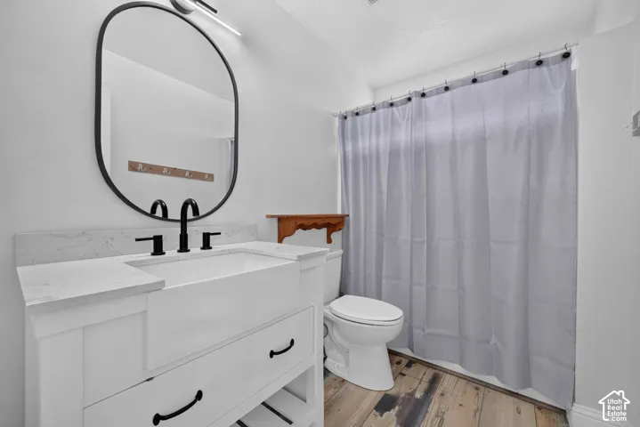 Modern vanity with a farmhouse-style sink, quartz countertop, matte black fixtures, and wood-finish flooring