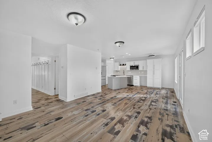 Wood-finish flooring, white walls, recessed lighting, white kitchen cabinetry, and a center island with a cooktop