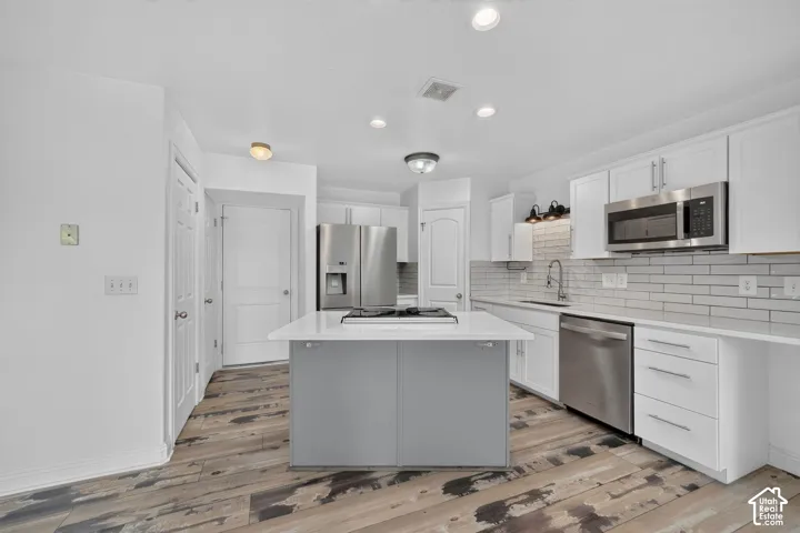 Kitchen featuring white cabinetry, stainless steel appliances, a center island with a cooktop, subway tile backsplash, and wood-finish flooring