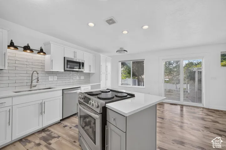 White shaker cabinetry with stainless steel appliances, light-toned subway tile backsplash, and wood-finish flooring