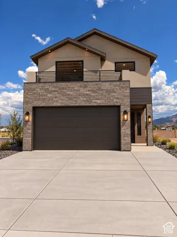Stucco and stone exterior featuring an integrated garage, upper-level balcony with metal railing, and recessed lighting