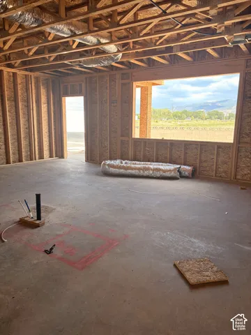 Unfinished interior framing with exposed ceiling joists and a large window opening, offering a distant mountain landscape