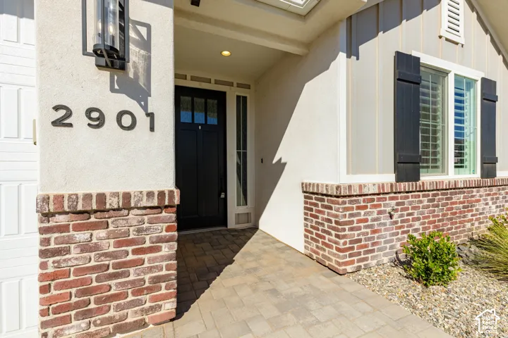 Stucco exterior with brick detailing, dark paneled front door, paver walkway, and black exterior light fixture