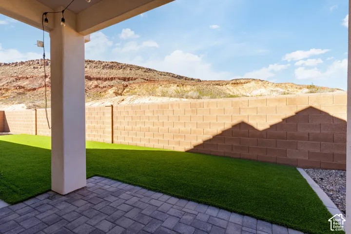 Covered patio featuring paver flooring, artificial turf, and block wall fencing