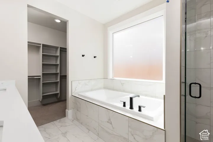 White soaking tub with matte black fixtures, marble-style tile surround, and an adjacent walk-in closet with built-in shelving