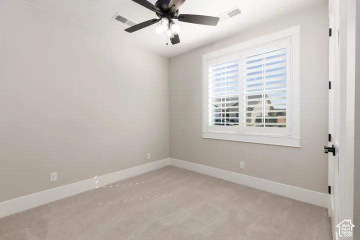 Bright, light-filled bedroom showcasing neutral carpeting, crisp white trim, and a ceiling fan with integrated lighting