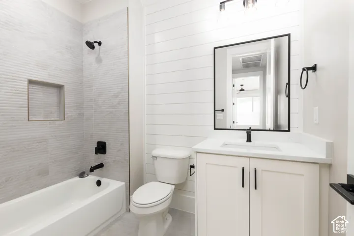 White subway tile shower surround with integrated niche, white bathtub, shiplap accent wall, white vanity with stone countertop, and matte black fixtures
