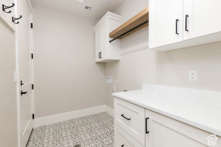 White cabinetry with matte black hardware, light-toned countertop, wood-finish shelving, and patterned floor tiling