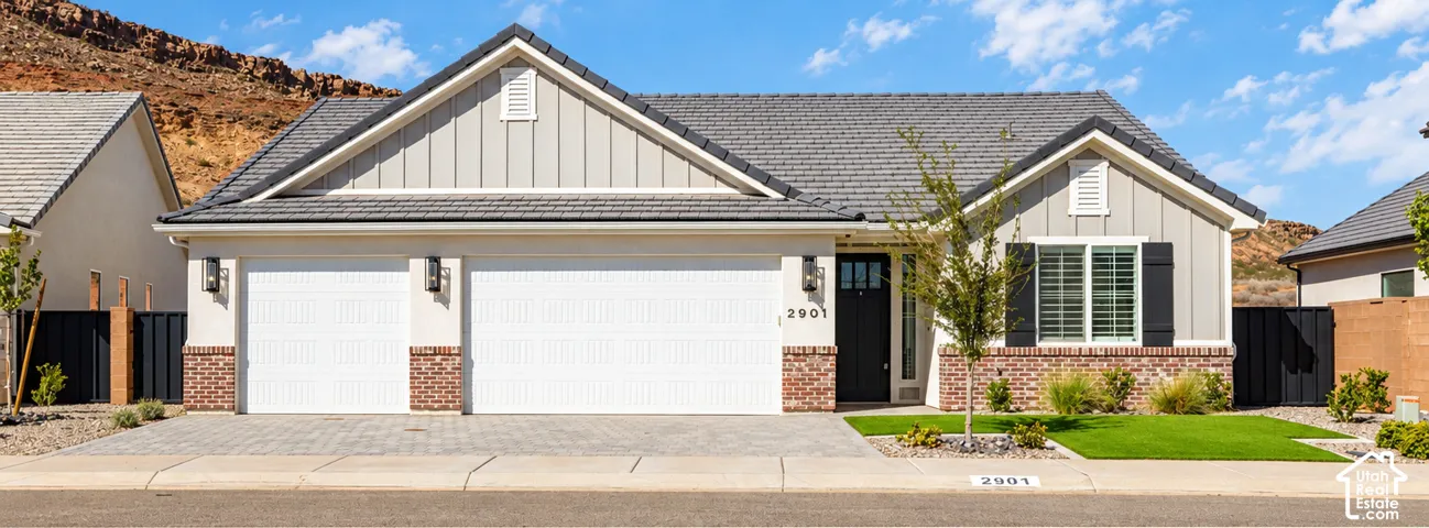 Light-toned exterior with brick accents, multi-car garage, dark-toned roof, and a landscaped front yard