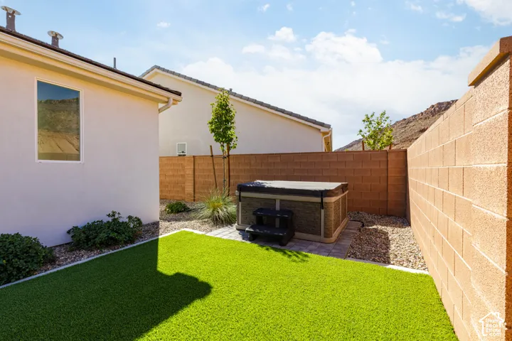 Private backyard featuring artificial turf, a hot tub on a paver patio, and low-maintenance landscaping with decorative rock