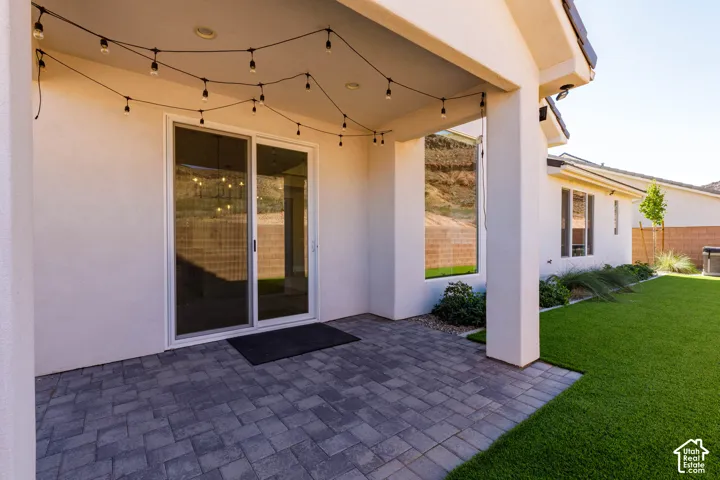 Covered patio with string lighting, paver stone hardscaping, sliding glass door, and a manicured lawn