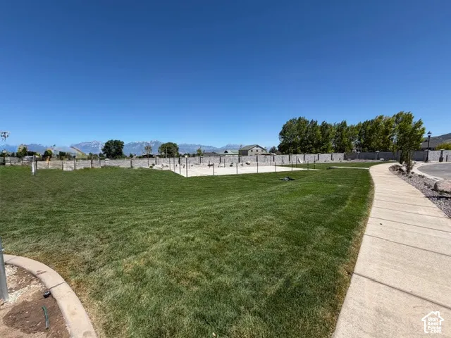 Expansive green space featuring a concrete pathway, a sand court, and a perimeter wall