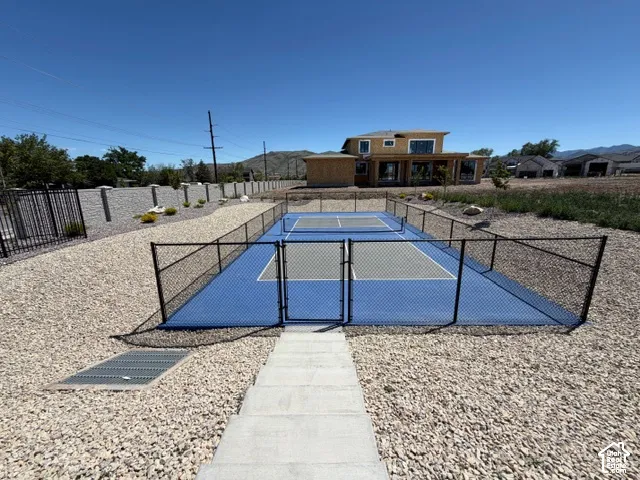 Fenced court with blue and gray playing surfaces, surrounded by gravel landscaping and a retaining wall
