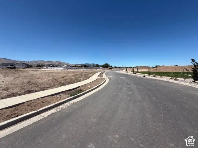 Paved street and concrete sidewalk with surrounding land and distant mountains