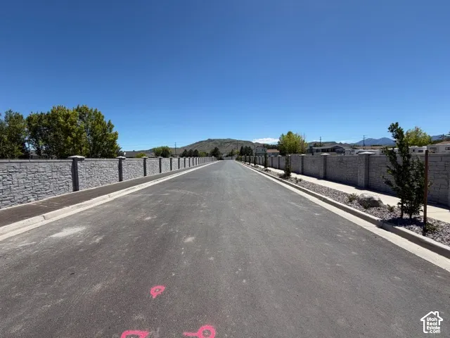 Paved road with curbs, concrete sidewalks, and a stone-finish privacy wall
