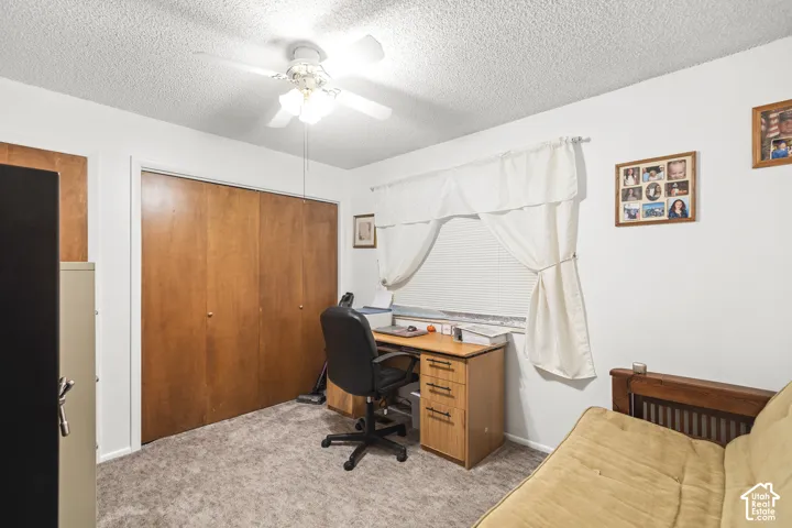 Wood-finish bi-fold closet doors, textured ceiling, ceiling fan, and carpet flooring