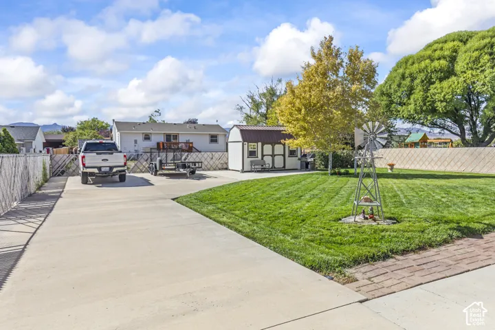 Expansive concrete driveway, mature lawn with a decorative windmill, and a storage shed with a metal roof