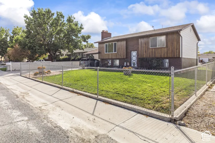 Two-story residence featuring brick and vertical wood siding, a chimney, and a chain-link fence enclosing a green lawn