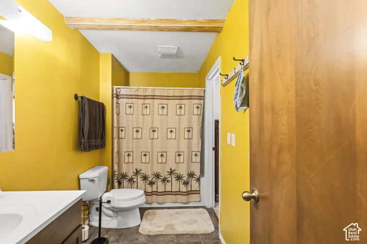 Bathroom featuring a white vanity with integrated sink, toilet, and shower with a curtain rod