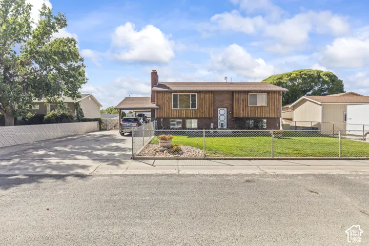 Brick and wood-sided exterior with a covered carport, fenced front yard, and a paved driveway