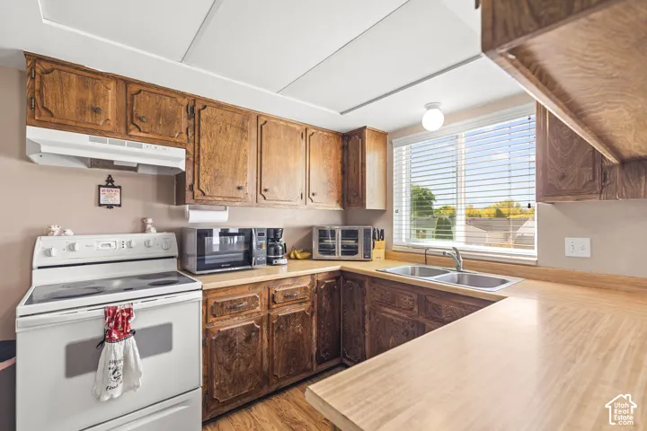 Wood-finish cabinetry, dual basin stainless steel sink, large window, and light-toned countertops