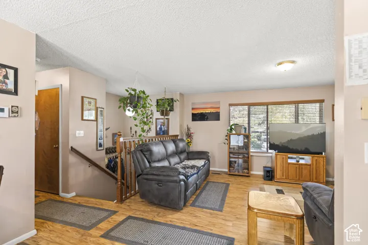 Living area with wood-finish flooring, a wood banister, and a large window with blinds