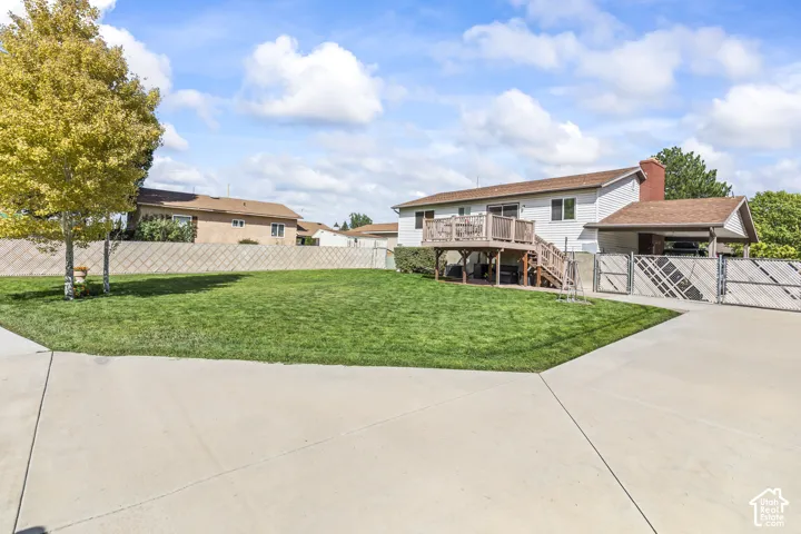 Expansive concrete driveway, large green lawn, and multi-level rear wood deck with railing