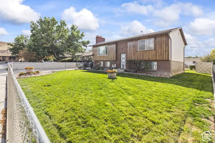 Expansive front lawn with a chain-link fence, brick and wood-panel exterior, and mature landscaping