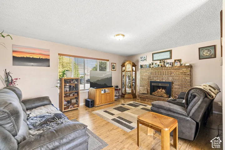 Living area featuring a brick fireplace, wood-finish flooring, and natural light from a window with blinds