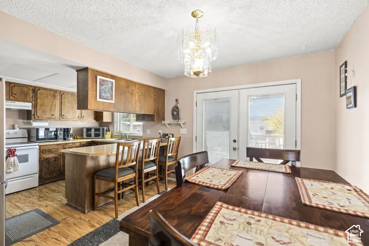 Kitchen featuring wood-finish flooring, wood cabinetry, a breakfast bar with seating, a gold-toned chandelier, and white French doors