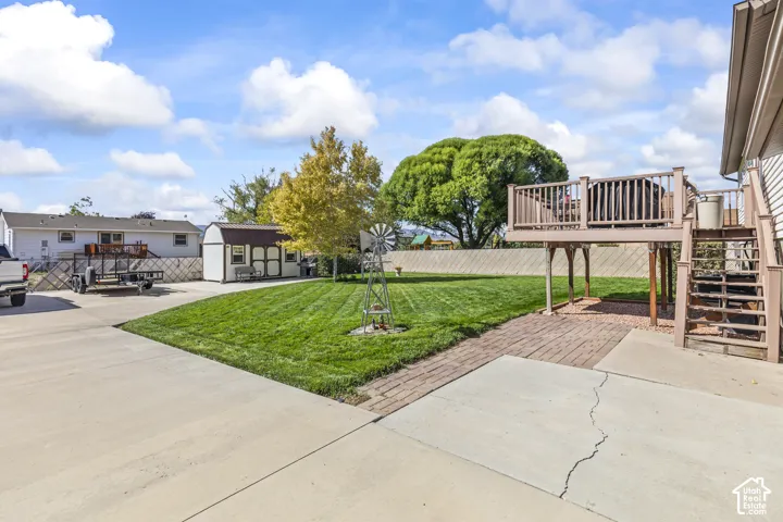 Expansive green lawn, elevated wood deck with railing, exterior storage shed, concrete driveway, and brick paver patio