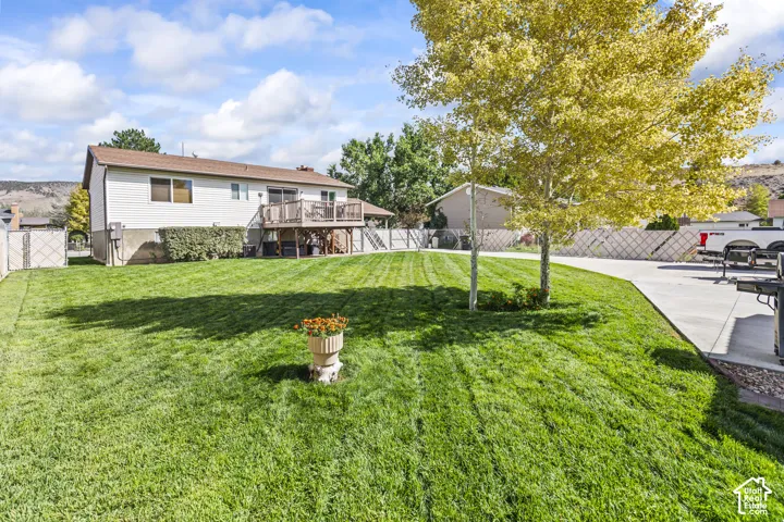 Expansive green lawn, multi-level wood deck, concrete patio, mature trees, and privacy fencing