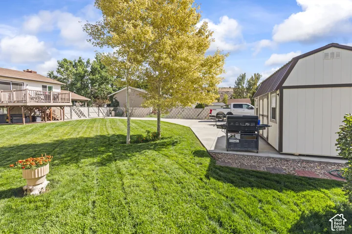 Expansive green lawn, elevated wood-finish deck with railings, concrete driveway, and a detached shed with a brown metal roof