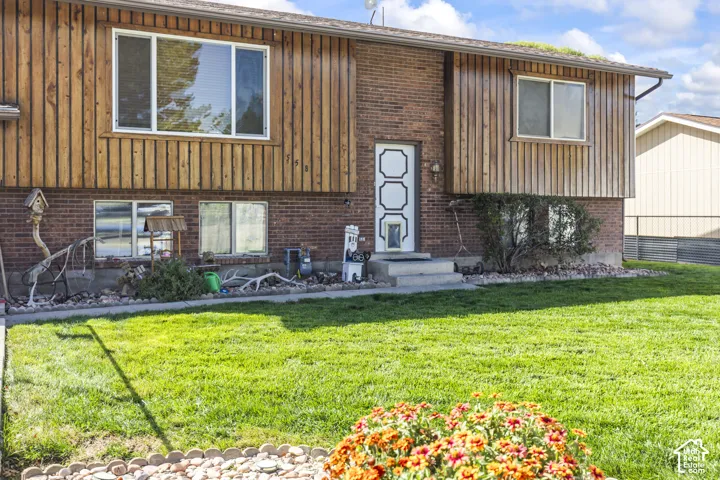Brick and vertical wood siding exterior with a white entry door, multi-pane windows, and a concrete entry pad