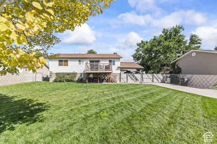 Expansive backyard featuring a manicured lawn, an upper-level deck with wood railing, a lower-level patio, and a paved driveway