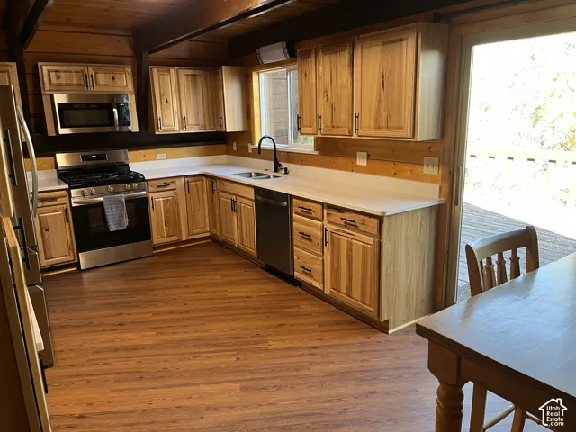 Wood-finish flooring, light wood cabinetry, stainless steel appliances, white countertops, and a sliding glass door to exterior decking