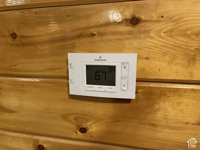 Digital thermostat with a white finish, mounted on a wood-paneled wall
